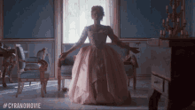 a woman in a pink dress is standing in a room with #cyranomovie