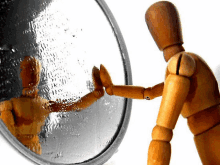 a wooden mannequin stands in front of a mirror and looks at his reflection