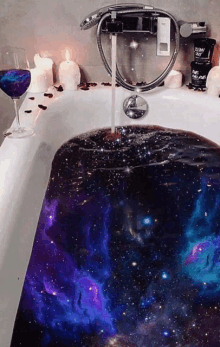 a bathtub with a galaxy design on the floor and a glass of wine