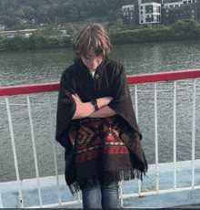 a person wearing a poncho standing on a bridge overlooking a body of water