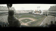 a man in a plaid shirt stands in front of a baseball stadium with a scoreboard that says giants on it