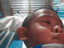 a young boy laying on a blue and white striped bed looking at the camera