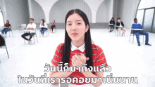 a girl in a red shirt stands in front of a group of people in a classroom with foreign writing