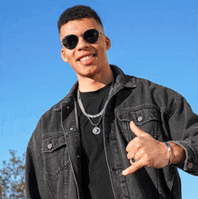 a young man wearing sunglasses and a denim jacket is giving a thumbs up