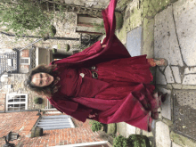 a woman in a red dress and cape is standing on a sidewalk