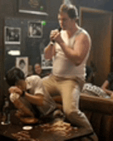 a man is singing into a microphone while sitting on a table in a bar .