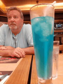 a man sits at a table next to a glass of blue liquid with ice