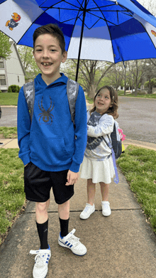 a boy and a girl are standing under a blue umbrella with a falcon on it