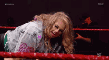 a woman in a denim jacket is in a wrestling ring with nxt uk written on the bottom