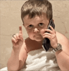 a baby wrapped in a towel is talking on a cell phone .