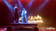 a man in a top hat stands on a stage in front of a fire behind him is a gif that says imgplay