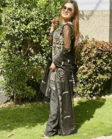 a woman in a black dress and sunglasses is standing in the grass