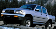 a silver toyota hilux pickup truck is parked on rocks near a river