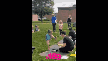 a man is kneeling down in front of a group of children in a park with the number 190 on the ground .