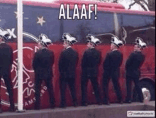 a group of men are urinating in front of a red bus with the word alaaf written on it .