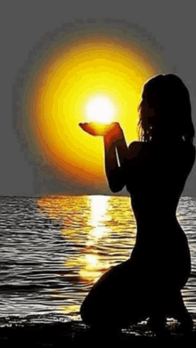 a woman is kneeling in the water holding the sun in her hands in front of the ocean .