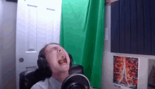 a man wearing headphones is crying in front of a green curtain and a picture of the eiffel tower