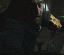 a man with a beard is eating a slice of pizza in a dark room with the letters aa on the bottom right