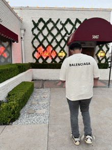 a man wearing a balenciaga t-shirt stands in front of a drake 's restaurant