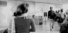 a black and white photo of a woman standing in front of a crowd of people at an airport .