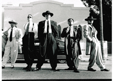 a group of men in suits and hats standing on a street