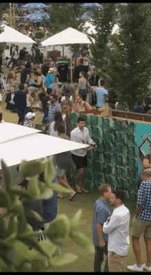 a crowd of people are gathered in a field with a green wall in the background