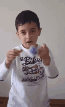 a young boy wearing a white shirt with the word bikes on it is holding a blue object in his hands .