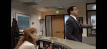 a man in a suit and tie is standing next to a woman at a reception desk in front of an exit sign