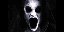 a woman with a scary face is screaming in the dark with her mouth wide open .