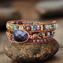 a bracelet with purple beads is sitting on a stone