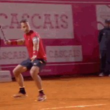 a man in a red shirt is swinging a tennis racquet on a tennis court in front of a sign that says cascais