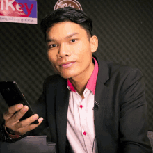 a man is holding a cellphone in front of a sign that says ikey tamil