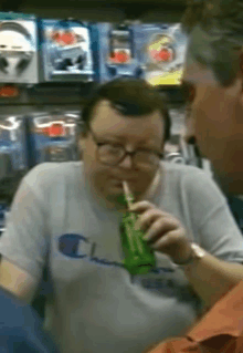 a man wearing glasses and a champion shirt drinks from a green bottle