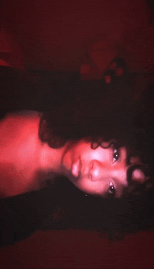 a woman with curly hair is laying down in a dark room with a red background