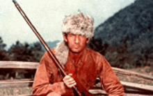 a man in a fur hat is holding a rifle while sitting on a bench .