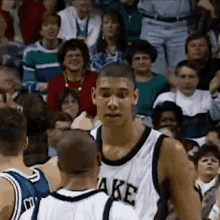 a basketball player wearing a white jersey with the word lake on it is standing in front of a crowd of people .