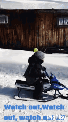 a child is riding a snowmobile in front of a wooden building with the words " watch out watch out watch out "