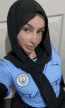 a woman wearing a manchester city shirt and a black scarf takes a selfie