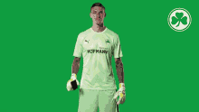 a man wearing a green hofmann jersey holds a pair of gloves