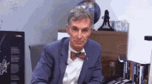 a man in a blue suit and bow tie is sitting at a desk in front of a globe .