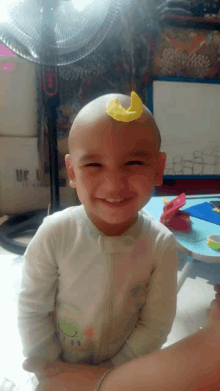 a baby with a yellow piece of paper on his head smiles for the camera