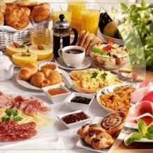 a table topped with a variety of food including croissants , sandwiches , fruit , and coffee .