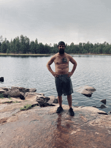 a shirtless man with a tattoo on his chest is standing on a rock near a lake