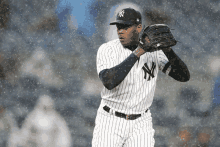 a man in a ny yankees uniform is standing in the rain