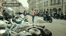 a man is walking down a street next to a row of motorcycles parked on the side of the road .