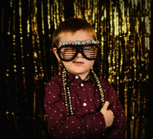 a young boy wearing glasses that say happy new year is standing in front of a gold curtain .