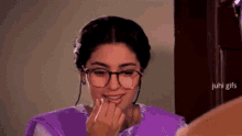 a woman wearing glasses and a purple dress is applying makeup to her lips .