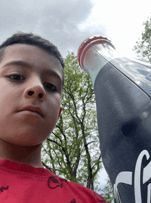 a young boy in a red shirt is holding a large coca cola bottle