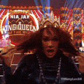 a woman with a crown on her head stands in front of a sign that says queen of the ring