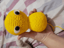 a person is holding a crocheted yellow object with big eyes